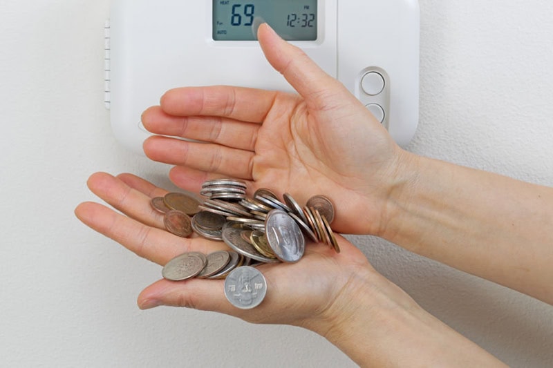 A person's hands in front of a thermostat holding change.